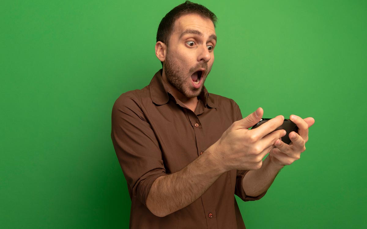 surprised young man holding looking mobile phone isolated green wall
